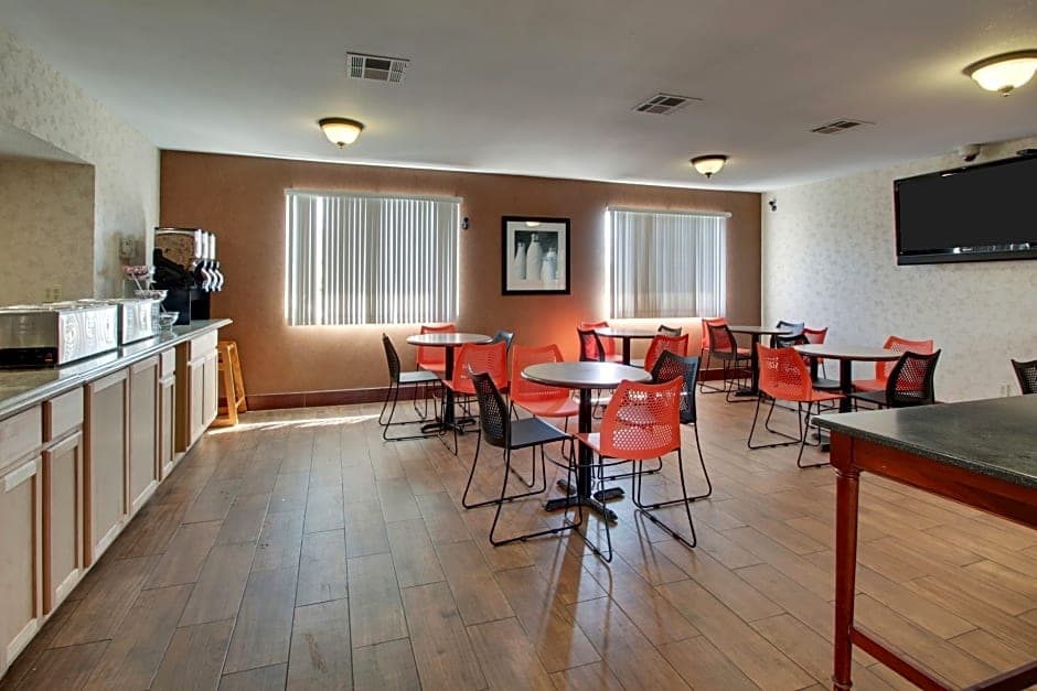 Bright breakfast area at Angel Inn Central in Branson MO with tables, colorful chairs, a coffee service counter, and wall mounted TV