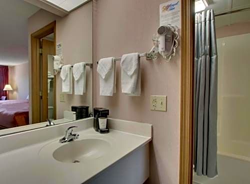 Bathroom vanity and tub shower area in a Queen Room at Angel Inn Central in Branson, MO, featuring a sink, mirror, hair dryer, towels, and shower curtain