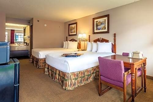 Two queen beds in a Branson MO hotel guest room with a desk, chair, TV, and vanity area at Angel Inn Central